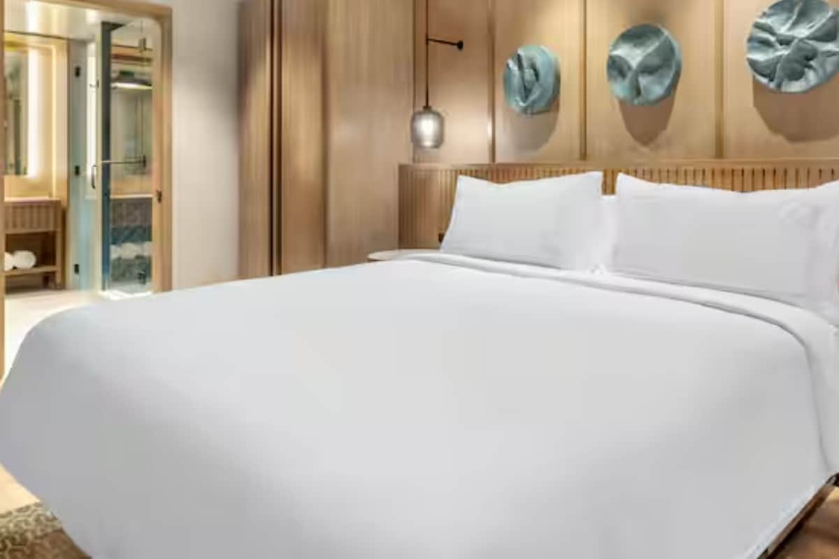 A large bed with white linens, a wooden headboard, and a round bedside table with a light fixture.