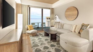 Ein modernes Wohnzimmer mit einer Couch, einem Couchtisch, einem Fernseher und einem großen Fenster mit Blick auf das Meer.