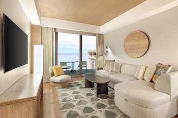 A spacious lobby with a high ceiling, wooden beams, and a central column. There are seating areas with woven chairs and a large abstract wall art piece. at Hilton Club Ka Haku Honolulu