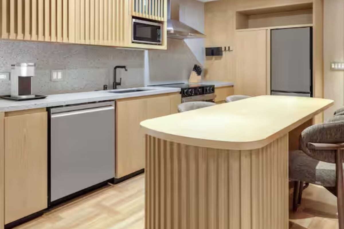 A modern kitchen with a central island, bar stools, a microwave, and a stove.