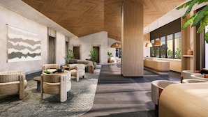 Eine geräumige Lobby mit hoher Decke, Holzbalken und einer zentralen Säule. Es gibt Sitzbereiche mit gewebten Stühlen und einem großen abstrakten Wandkunstwerk.