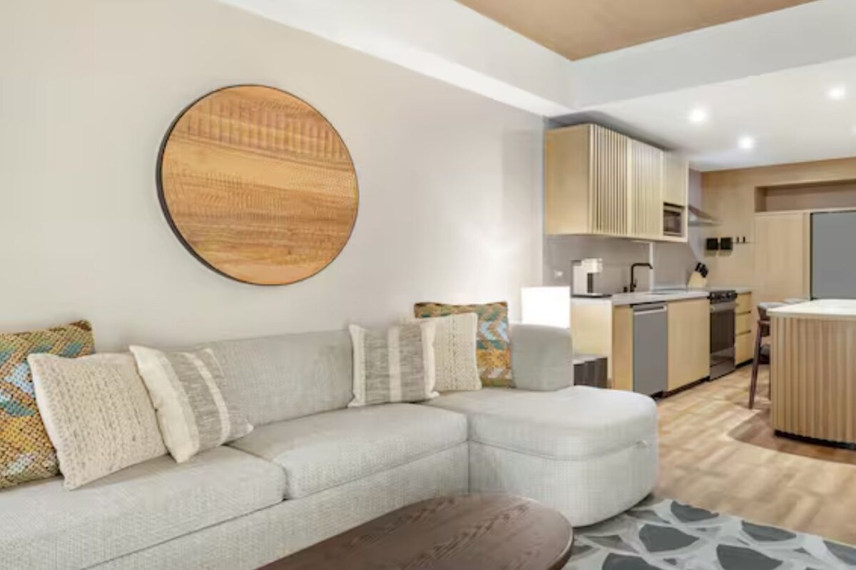 A modern living room with a sectional sofa, a round coffee table, and a kitchen area with a bar.