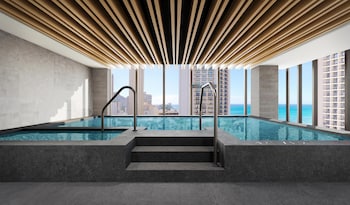 A modern hotel room with a wooden dining table, comfortable seating, a flat-screen TV, a ceiling fan, and a view of the ocean. at Hilton Club Ka Haku Honolulu
