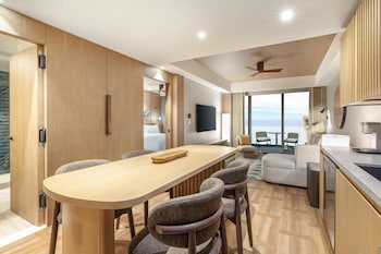 A modern hotel room with a wooden floor, a flat-screen TV, a sofa, a coffee table, and a view of the sea. at Hilton Club Ka Haku Honolulu