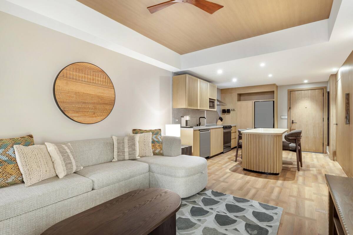 Een moderne woonkamer met een modulaire bank, een ronde salontafel en een keuken met een centraal kookeiland.