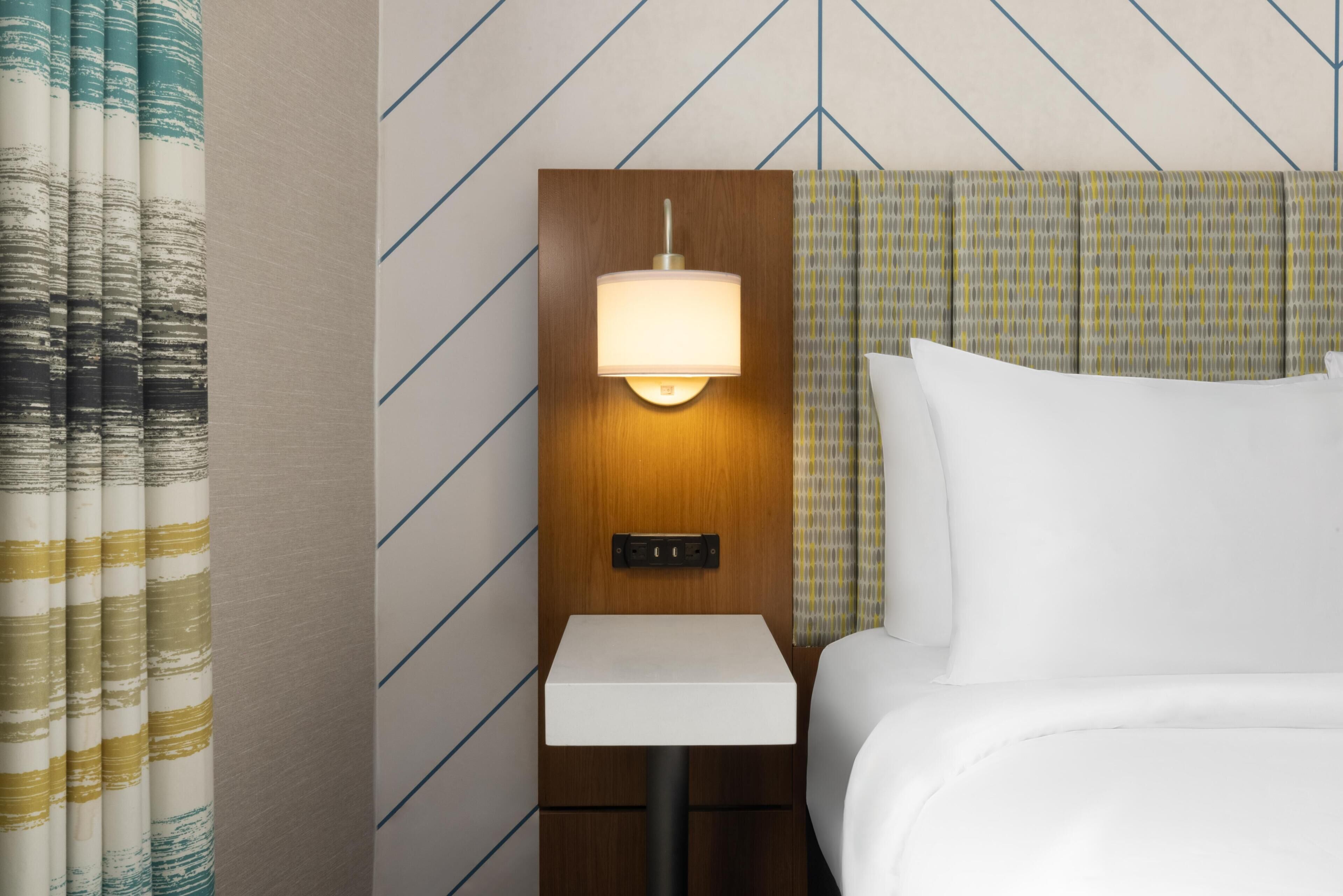 Une chambre d’hôtel avec un lit, une table de chevet avec une lampe et un mur orné d’un motif géométrique.
