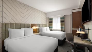 A hotel room with two beds, a desk with a lamp, a chair, and a TV.