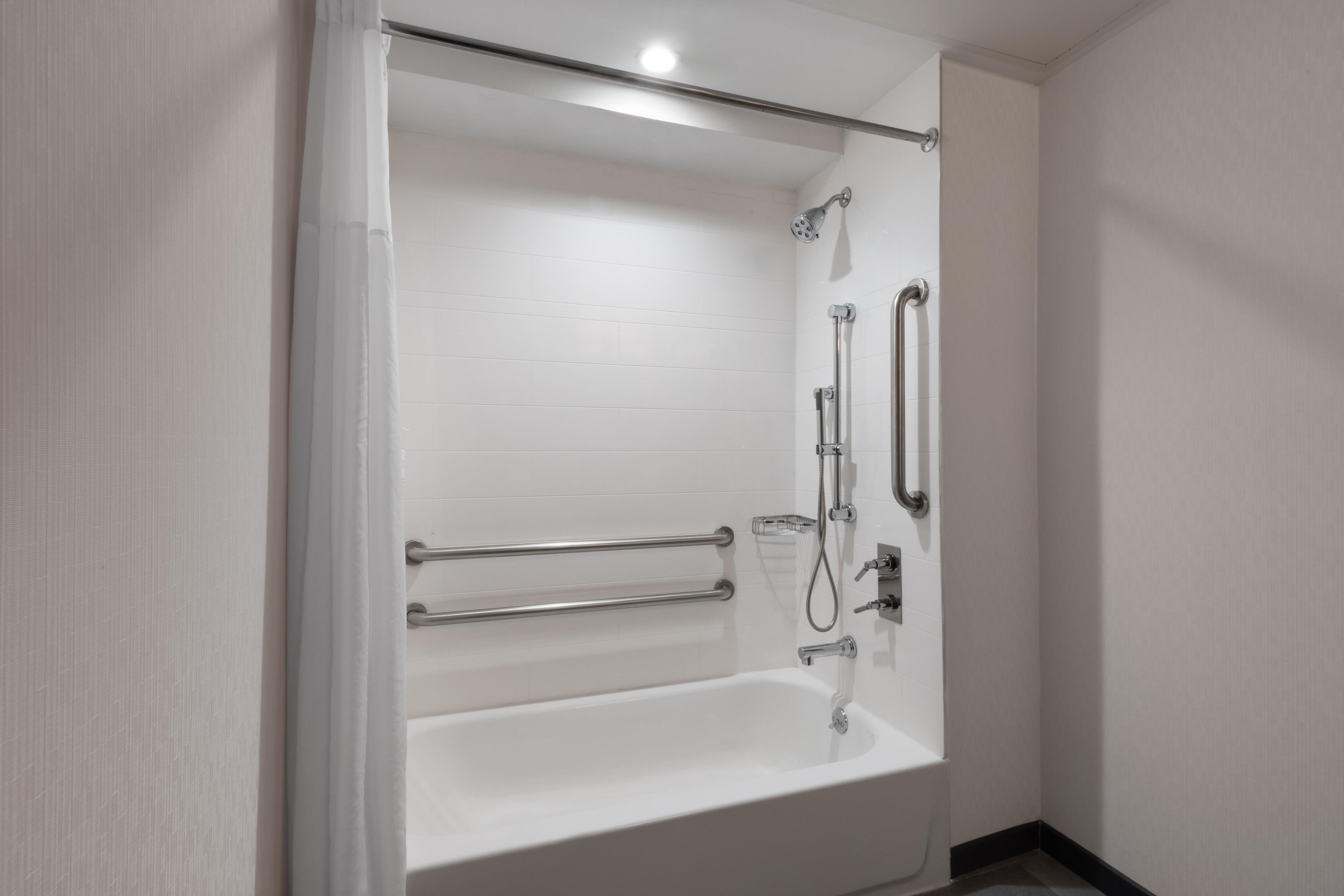 A modern bathroom with a white bathtub, grab bars, a showerhead, and a handheld shower attachment.