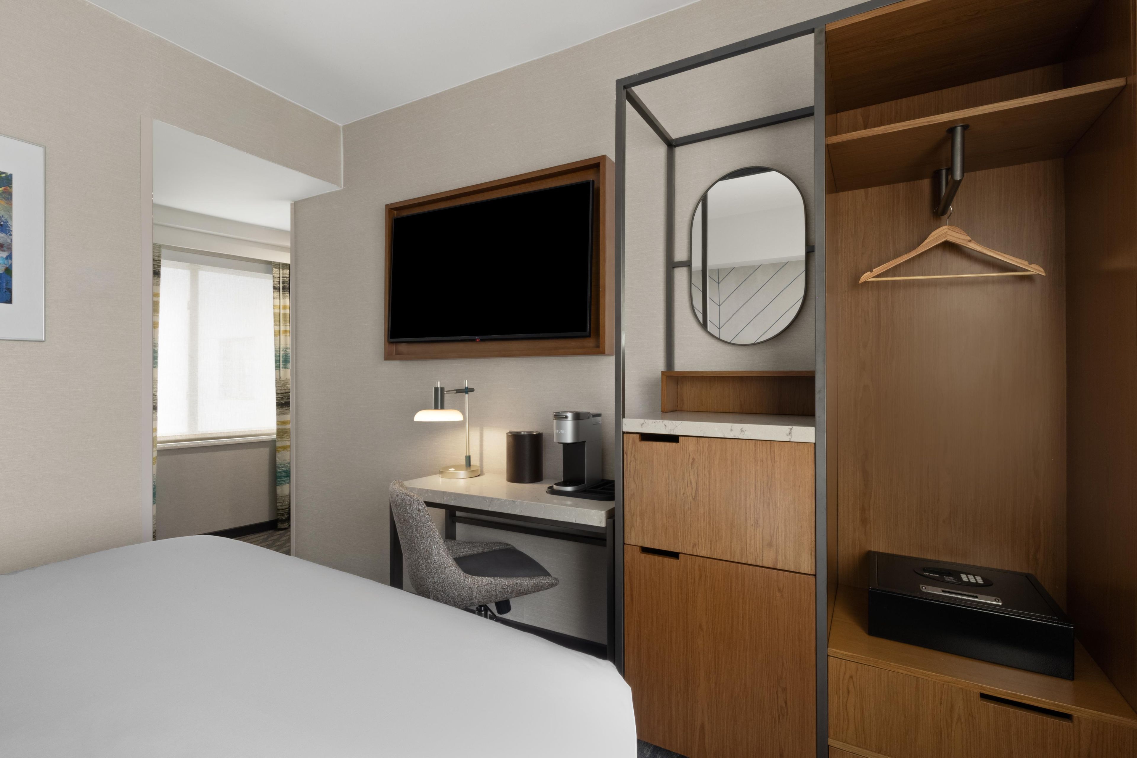 Een hotelkamer met een bed, bureau, stoel, kledingkast, spiegel en een televisie.