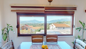 A dining area with a table, chairs, and a view of buildings and mountains through large windows. - Villa in Kavac with beautiful sea view (Kavač)