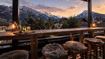 Eine Holzterrasse mit Barhocker und Blick auf schneebedeckte Berge.