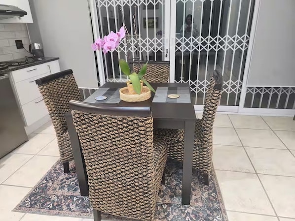 A dining area with a dark wooden table and woven chairs, a potted plant, and a decorative mirror.
