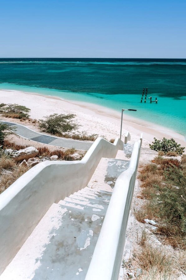 Ein Strand mit einem weißen, sandigen Pfad, der zum Wasser führt, einem klaren, blauen Himmel und einer ruhigen See.