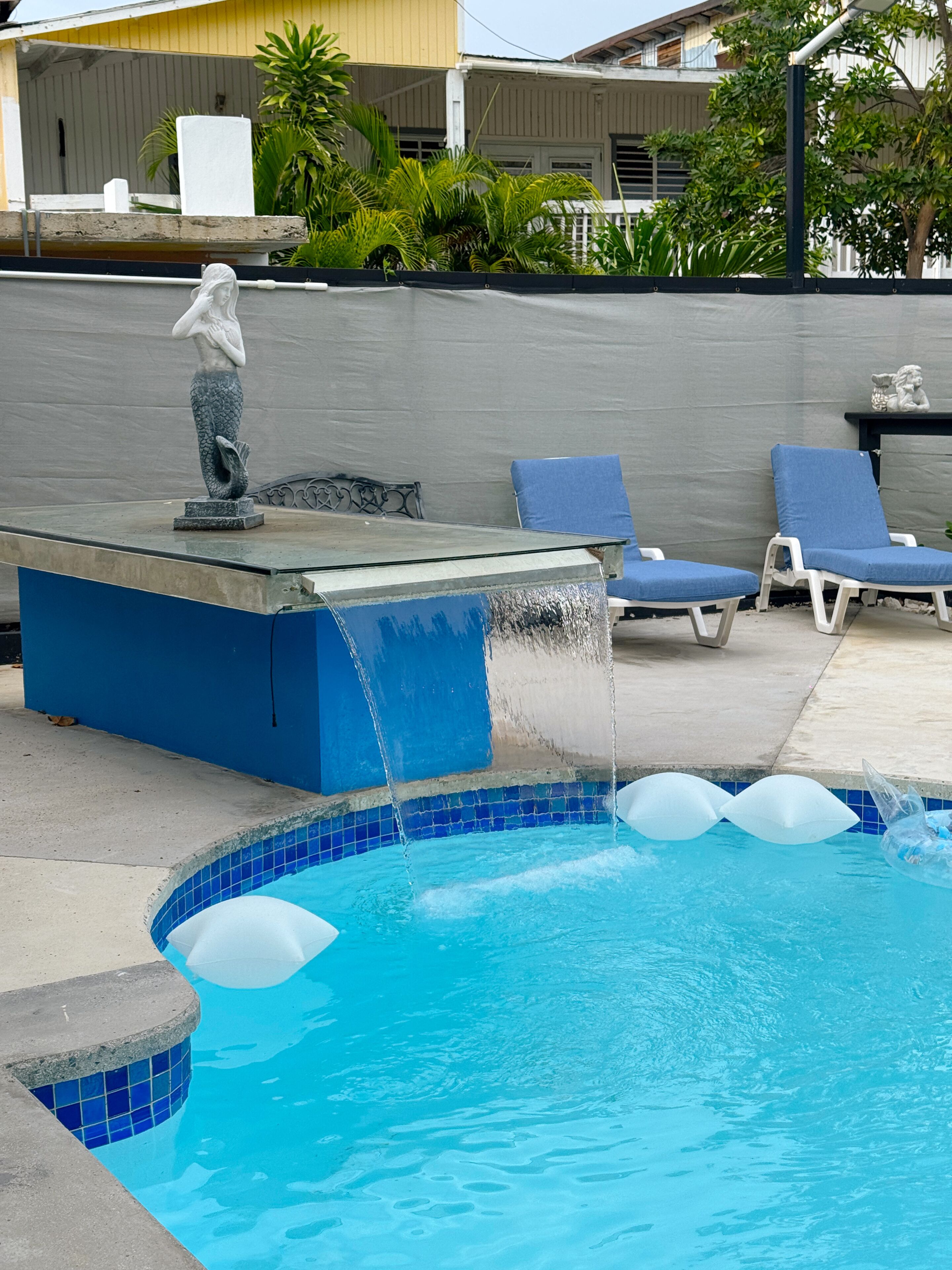 A swimming pool with a water feature, lounge chairs, and a statue.