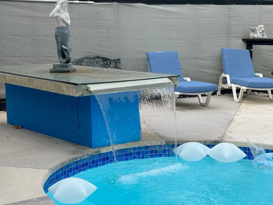 A swimming pool with a water feature, lounge chairs, and a statue.