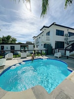 A swimming pool with a person in the water, surrounded by a white building with multiple windows and air conditioning units.