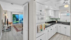 Cozinha moderna com armários brancos, bancada preta e vista para o exterior.
