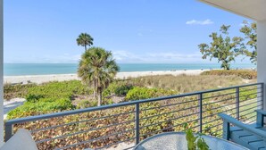Uma varanda com vista para a praia, uma palmeira e uma cerca.