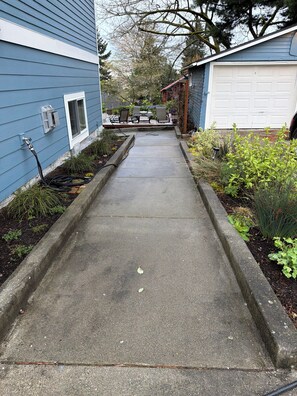 A concrete pathway leading to a patio area with outdoor furniture and a garage. - Garden-Level 2BR Suite, West Seattle (Seattle)