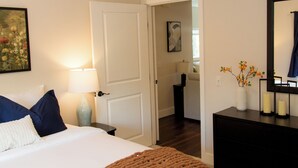 Une chambre à coucher comprenant un lit, une table de chevet, une commode, un miroir et une porte donnant sur une autre pièce.
