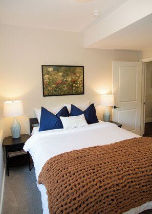 Une chambre d’hôtel avec un lit, deux lampes de chevet, un tableau au mur et une porte.