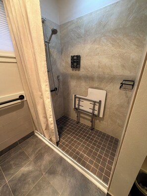 A shower with a curtain, a towel rack, and a wall-mounted soap dispenser. - Garden-Level 2BR Suite, West Seattle (Seattle)