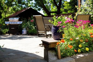 Un espace patio aménagé avec un barbecue, des sièges d’extérieur et une variété de fleurs.