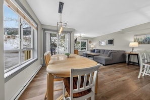 A modern living room with a dining area, large windows, and a view of the outdoors. - The Bunkhouse | Ski-in/Out | Central | Fireplace (Panorama)