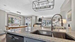 A modern kitchen with granite countertops, a dishwasher, a sink, and a dining area with a table and chairs. - The Bunkhouse | Ski-in/Out | Central | Fireplace (Panorama)