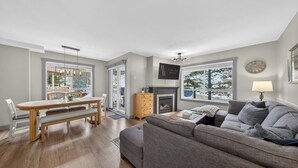 A living room with a fireplace, a sofa, a dining table, and a view of the outdoors. - The Bunkhouse | Ski-in/Out | Central | Fireplace (Panorama)