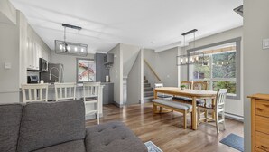 A modern kitchen with white cabinets, a dining area with a wooden table and chairs, and a staircase leading to an upper level. - The Bunkhouse | Ski-in/Out | Central | Fireplace (Panorama)