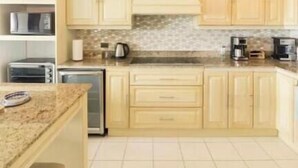 A kitchen with light wooden cabinets, a granite countertop, a hanging light fixture, and a tiled floor. - Oceanview Playa Blanca Apartment with Infinity Pool & Private Beach Access (Herradura)