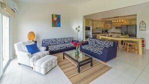 A modern living room with a sofa, armchair, and coffee table, a kitchen in the background, and a painting on the wall. - Oceanview Playa Blanca Apartment with Infinity Pool & Private Beach Access (Herradura)