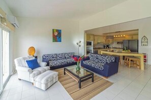 A modern living room with a sofa, armchair, and coffee table, a kitchen in the background, and a painting on the wall. - Oceanview Playa Blanca Apartment with Infinity Pool & Private Beach Access (Herradura)