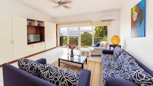 A living room with a sofa set, a coffee table, a TV, and a balcony with a view. - Oceanview Playa Blanca Apartment with Infinity Pool & Private Beach Access (Herradura)