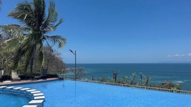 A swimming pool with a view of the ocean and palm trees. - Oceanview Playa Blanca Apartment with Infinity Pool & Private Beach Access (Herradura)