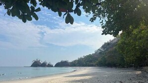 A beach with clear water, a sandy shore, and trees in the background. - Oceanview Playa Blanca Apartment with Infinity Pool & Private Beach Access (Herradura)