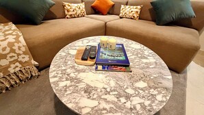 A living room with a brown sofa, two pillows, a coffee table with books and candles, and remote controls. - Élégance Moderne à Gueliz 1 Bedroom and Living Room (Marrakech)