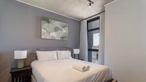 A modern hotel room with a large bed, two bedside tables with lamps, a large window, and a city view. - Golden Nectar (Cape Town)
