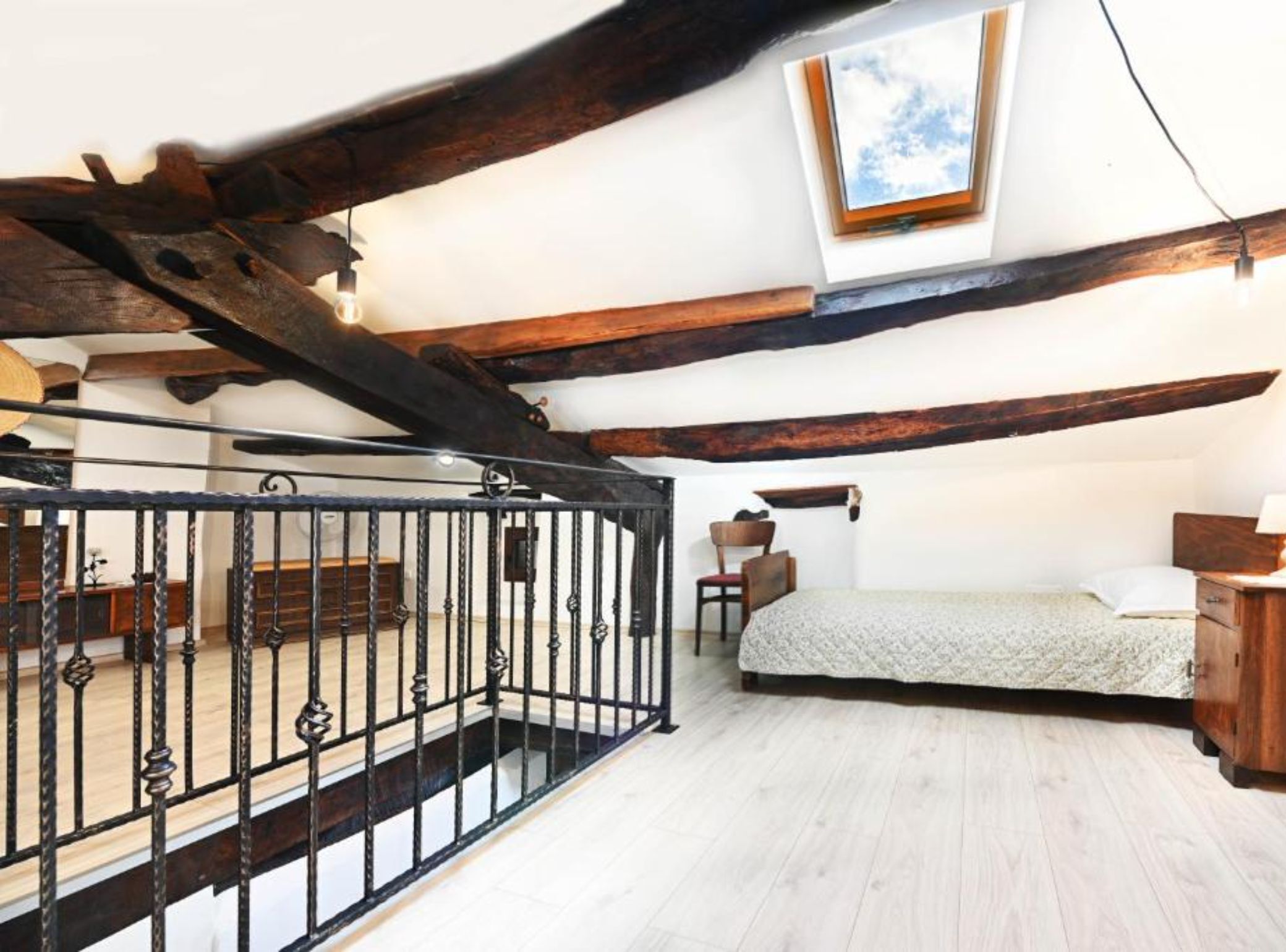 Un dormitorio con techo inclinado, una cama, una silla, un escritorio y una ventana.