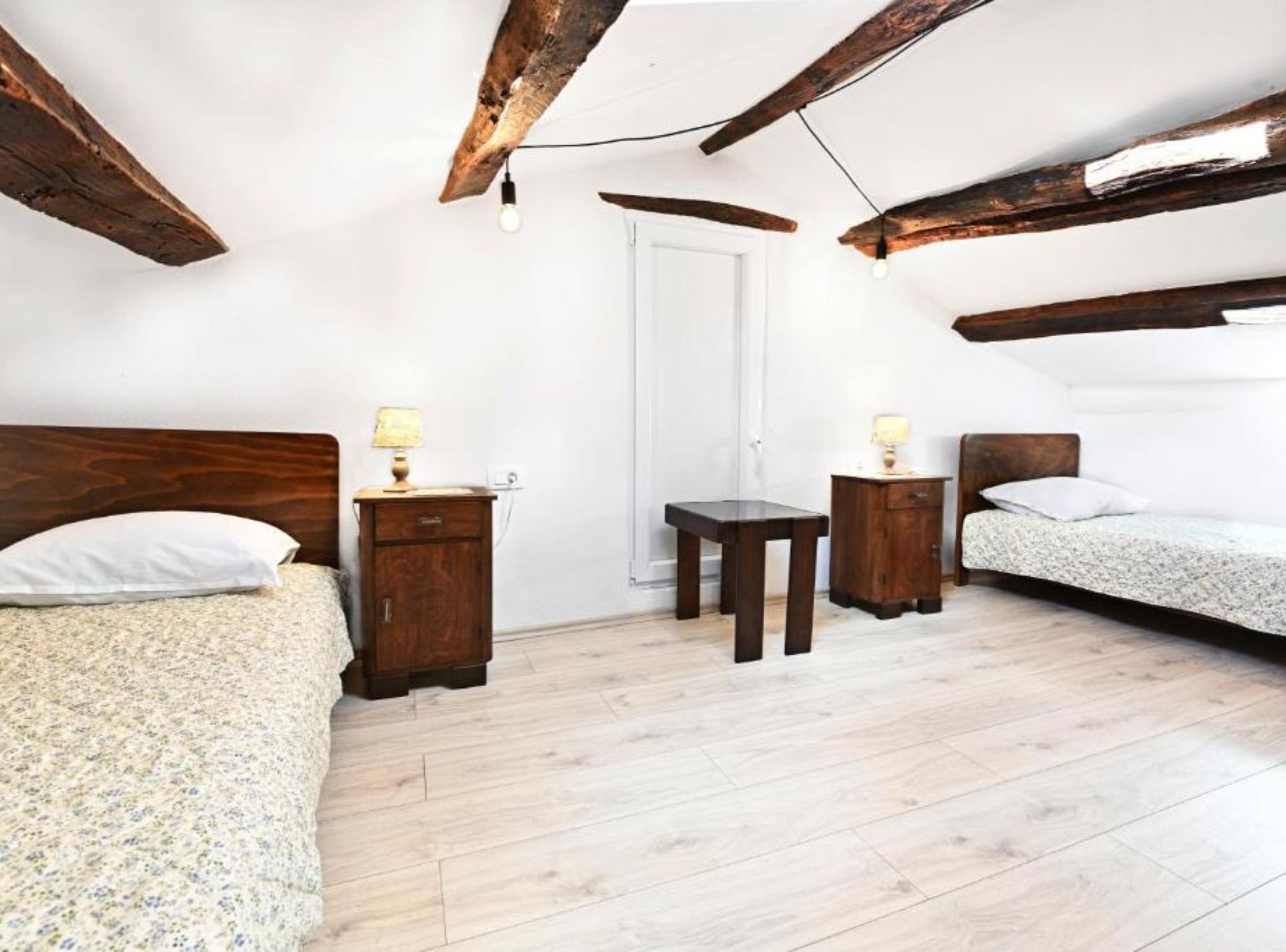 Ein Schlafzimmer mit Holzboden, zwei Nachttische mit Lampen, ein Bett mit Kissen und einer Tür.