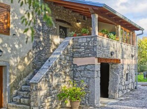 A stone building with a wooden staircase leading to a balcony, surrounded by greenery. - Baladur Nature Apartments (Buzet)