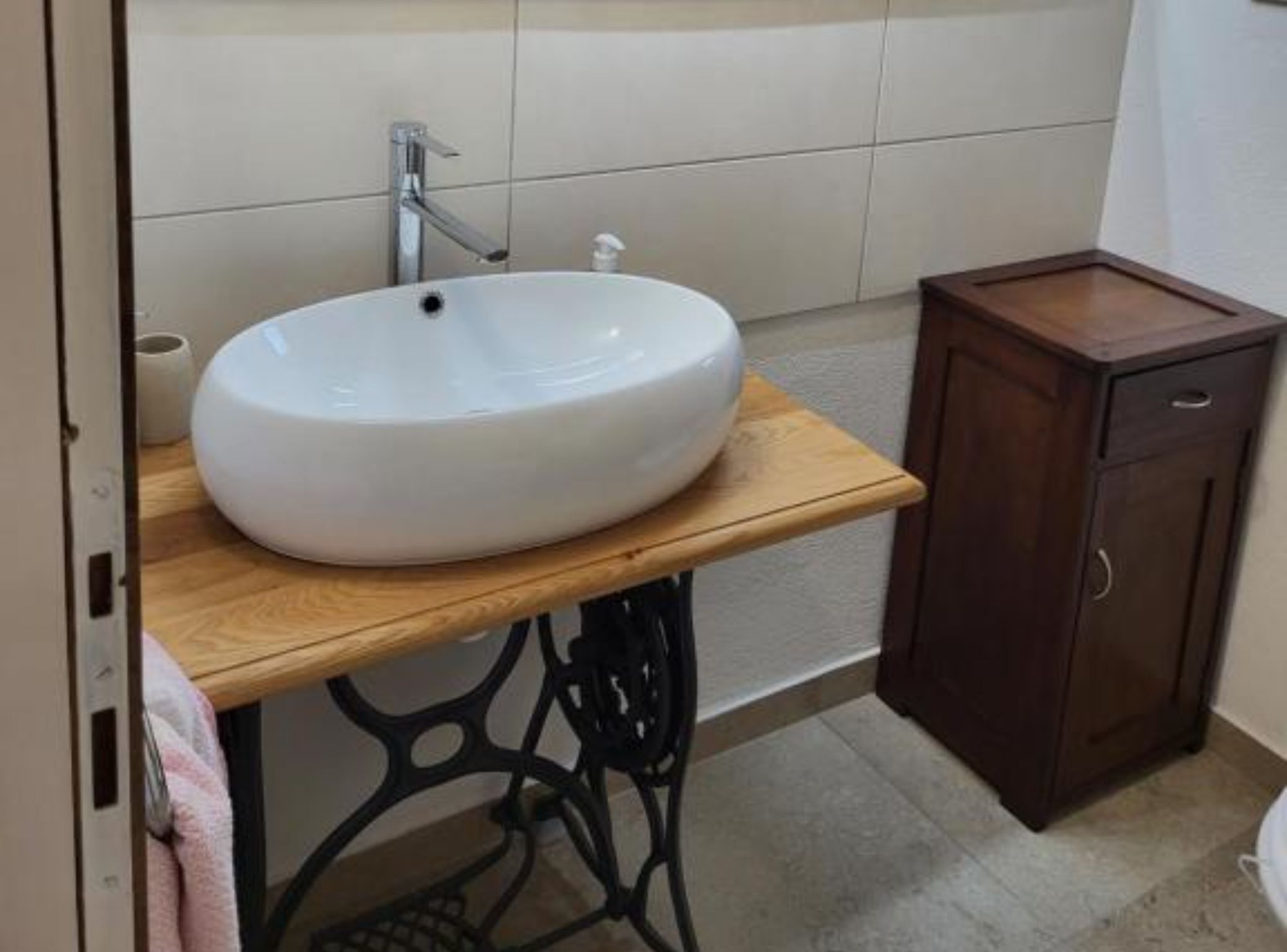 A bathroom with a white sink on a wooden vanity, a dark cabinet, and a tiled wall.