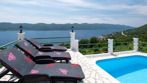A poolside area with lounge chairs and a view of a lake and mountains.