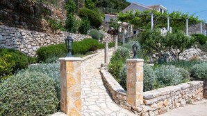 A stone pathway leading to a building with a stone wall and vegetation.
