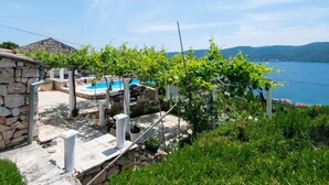 A stone house with a pool, surrounded by greenery and a view of a lake.