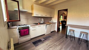 Eine Küche mit weißen Schränken, einem Gasherd, einem Geschirrspüler und einem roten Handtuch, das am Backofen hängt. Zwei Hocker und eine kleine Bar mit einer Ablagefläche sind vorhanden.