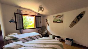 Ein Schlafzimmer mit zwei Betten, einem Fenster mit Vorhängen, einem Surfbrett und einem kissenförmigen Surfbrett.