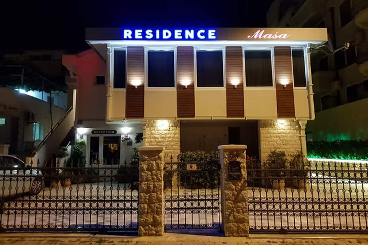 A building with a sign reading 'RESIDENCE' and 'Masa' at the entrance, a reception desk, and a gated driveway.