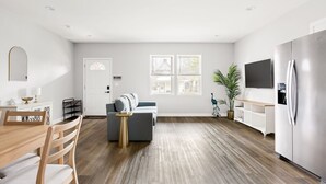 Ein modernes Wohnzimmer mit Essbereich, einem grauen Sofa, einem Holztisch und einem großen Flachbildfernseher.